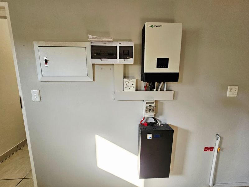 A clean utility area featuring a wall-mounted solar inverter, lithium battery storage system, and electrical distribution board.