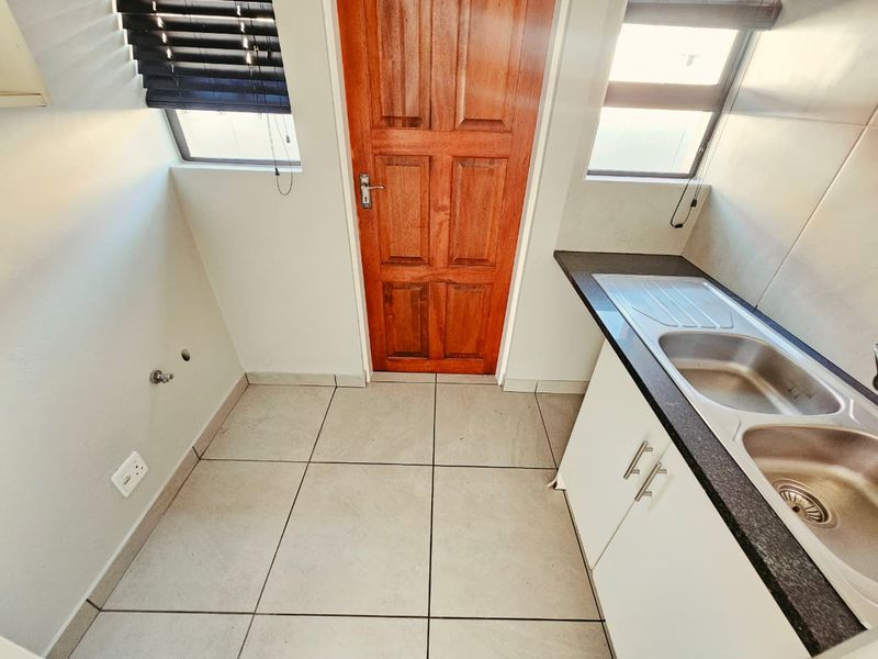A functional laundry room featuring tiled flooring, built-in base cabinetry with a double stainless steel sink, and plumbing connections for appliances.
