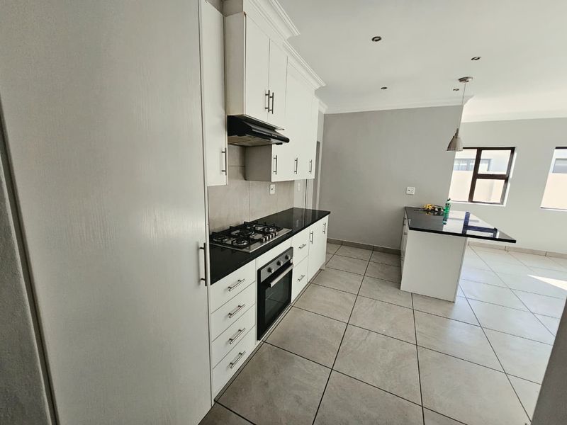 Modern kitchen featuring white cabinetry, granite countertops, a gas hob, built-in oven, and a functional island, set against neutral tiled flooring.
