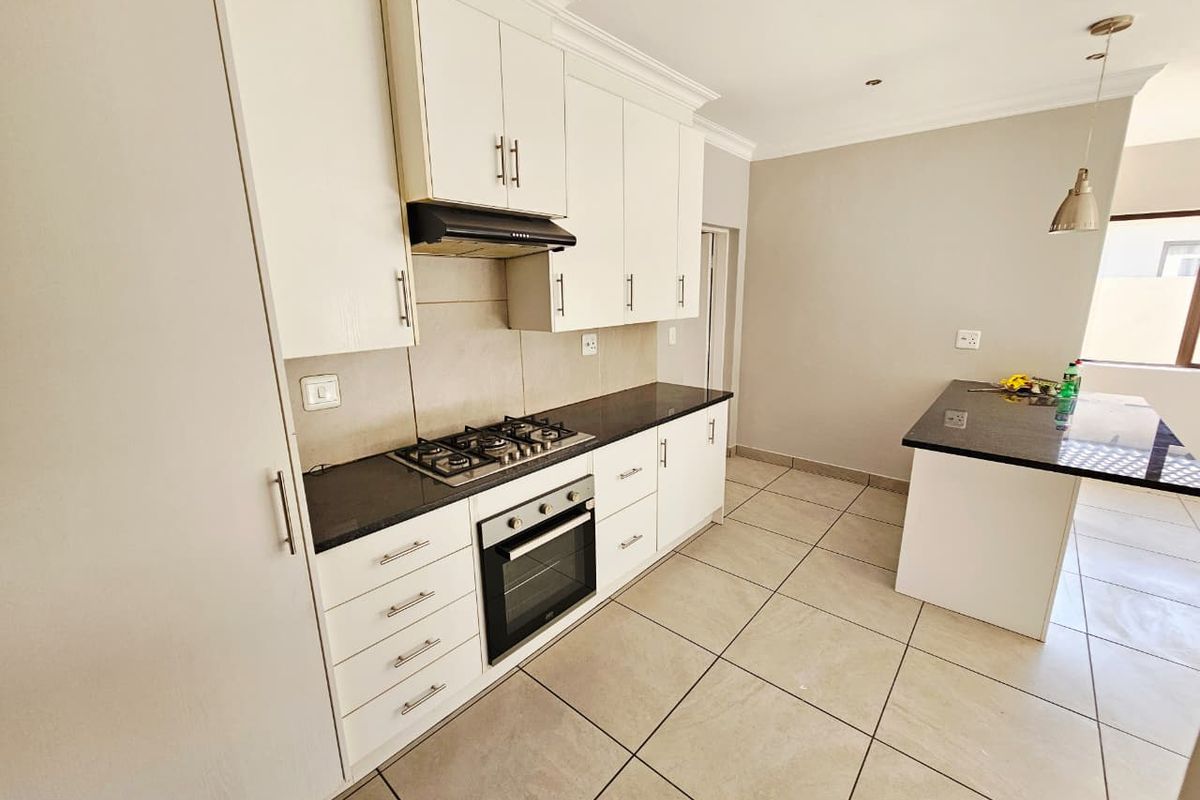 Modern kitchen featuring white cabinetry, granite countertops, a gas hob, built-in oven, and a central island, finished with neutral floor tiles.