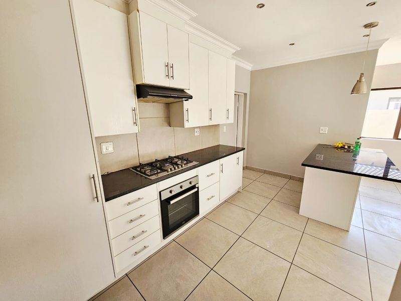 Modern kitchen featuring white cabinetry, granite countertops, a gas hob, built-in oven, and a central island, finished with neutral floor tiles.