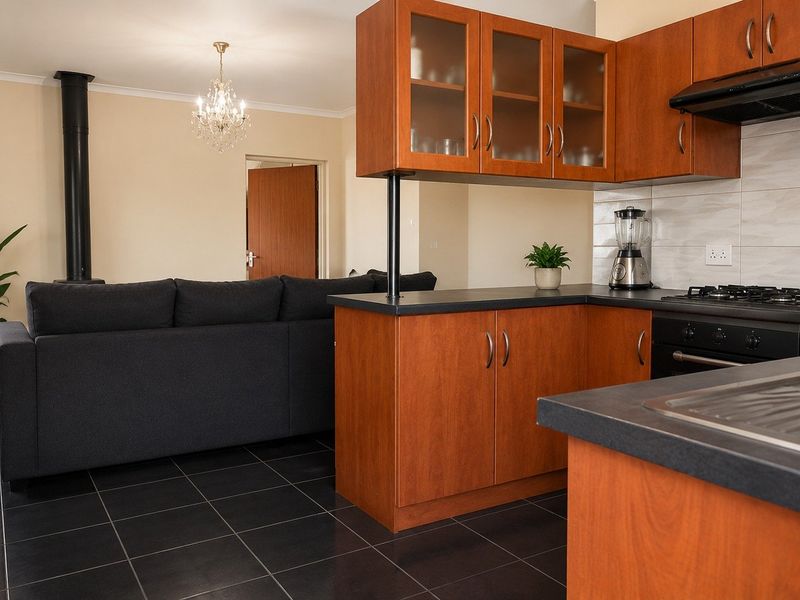 Open-plan kitchen featuring wood-look cabinetry, dark countertops, and a gas hob, seamlessly flowing into a living area with a freestanding fireplace.