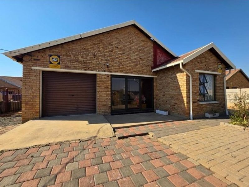 Front elevation of a face brick house featuring a single roller garage door, paved driveway, and aluminium window frames.