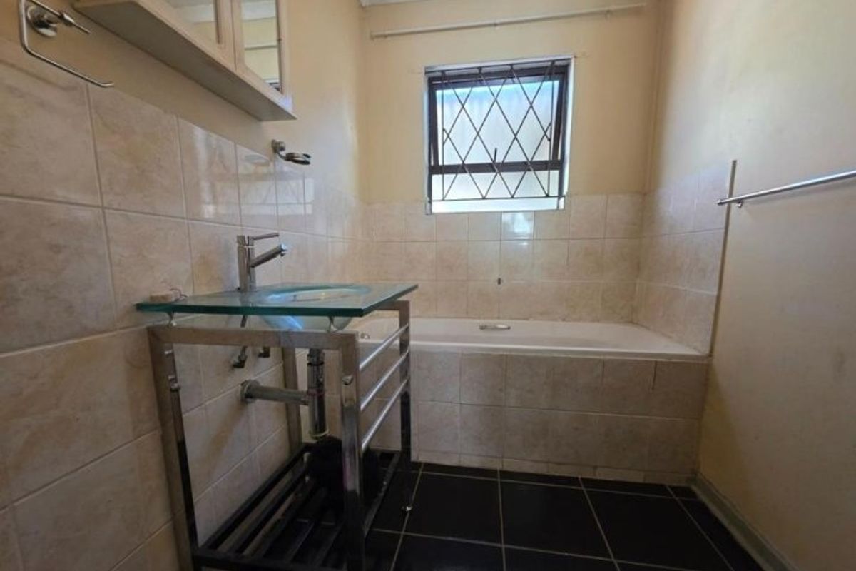 A functional bathroom featuring a bathtub, glass vanity basin, and tiled finishes, offering a blank canvas for modern renovation and aesthetic updates.