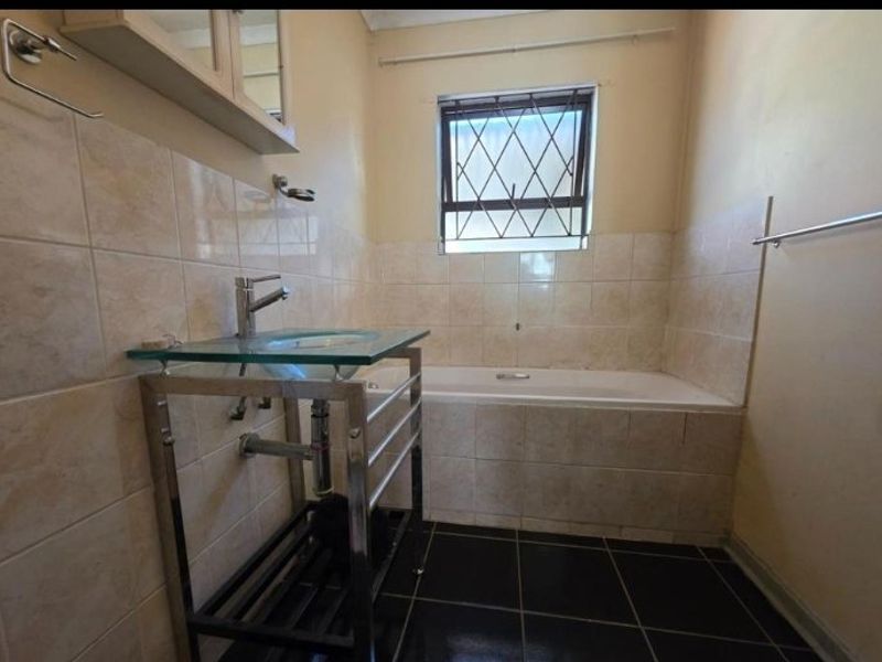 A functional bathroom featuring a bathtub, glass vanity basin, and tiled finishes, offering a blank canvas for modern renovation and aesthetic updates.