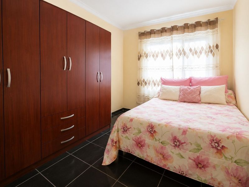 A well-maintained bedroom featuring dark wood built-in wardrobes, dark floor tiles, and neutral wall finishes.