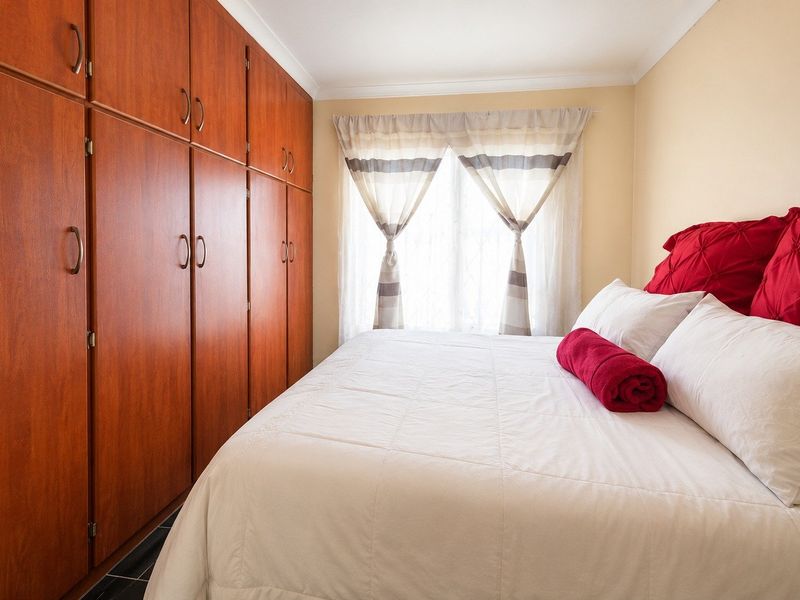 A bedroom featuring extensive floor-to-ceiling built-in wooden cupboards and natural light from the window.