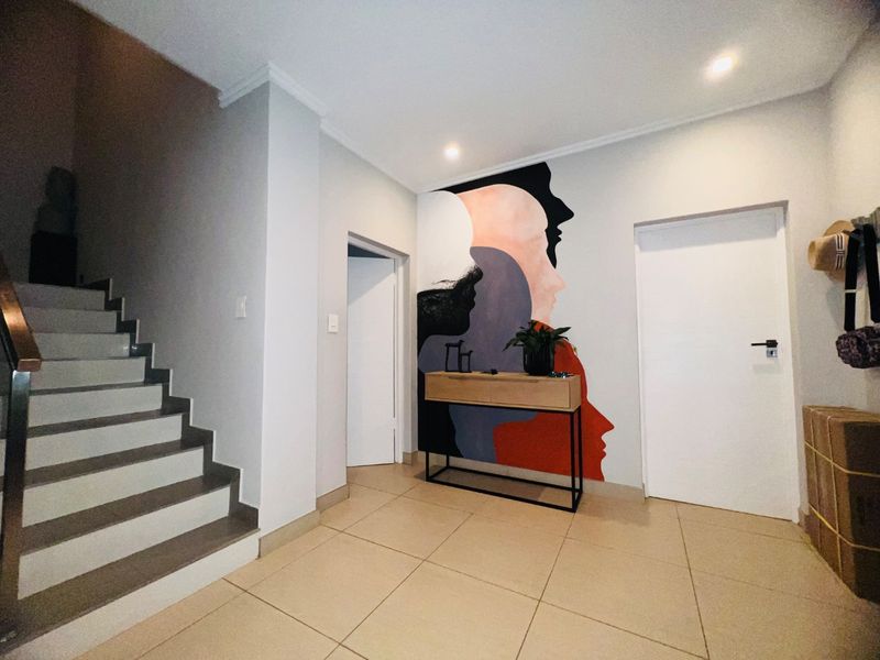 A bright and modern entrance hallway featuring tiled flooring, a staircase with modern finishes, and a decorative feature wall.