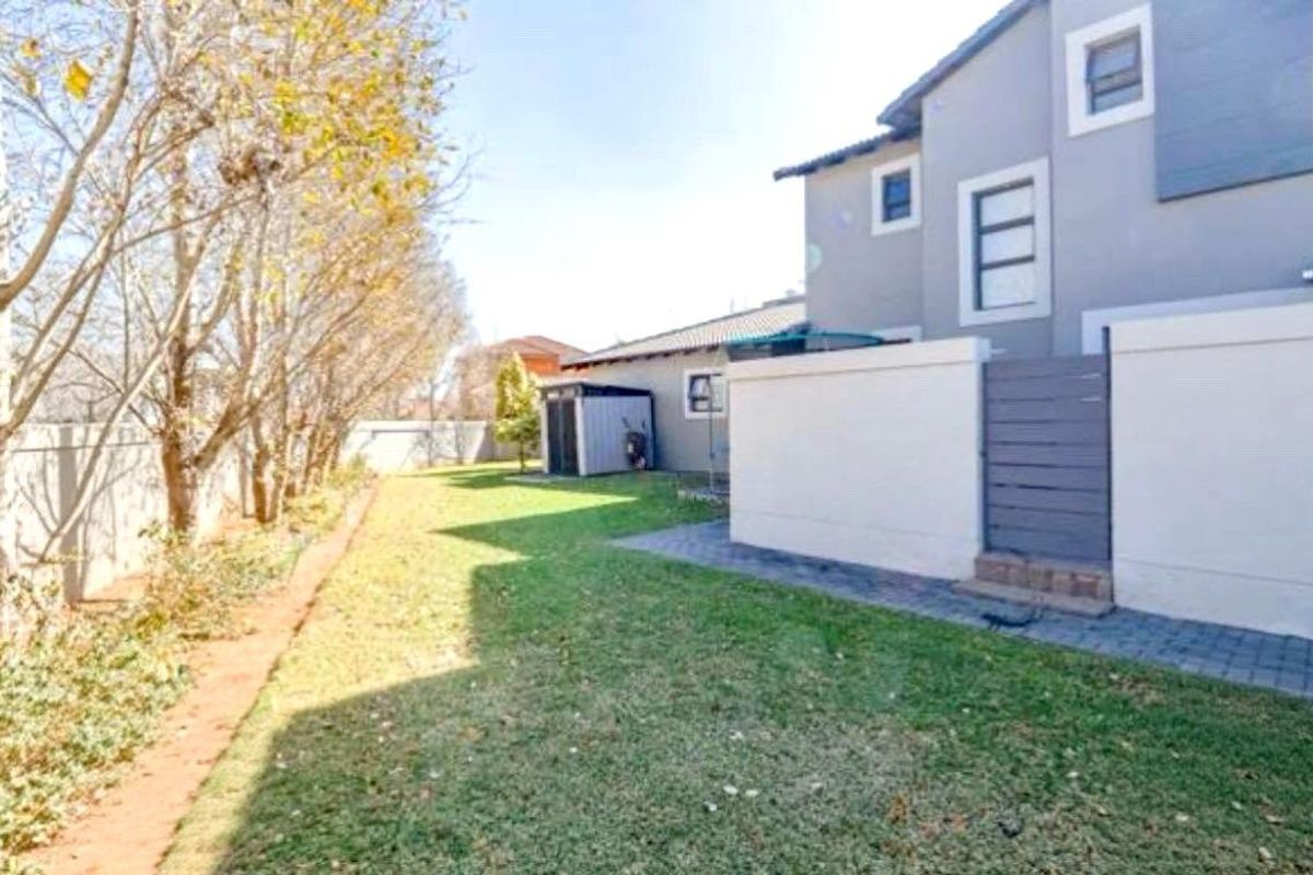 A view of the rear garden featuring a lawn, paved walkway, and boundary wall, providing a private outdoor space.