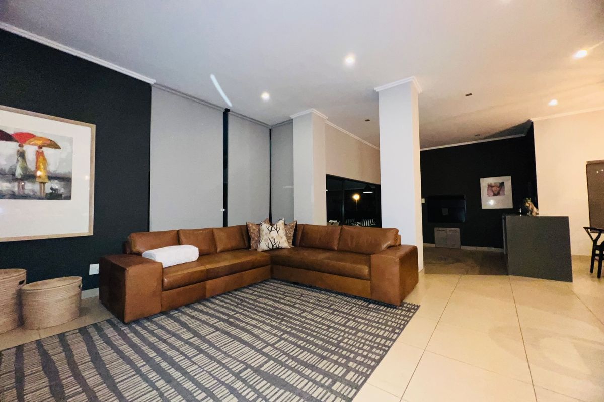Spacious living area featuring modern tiled flooring, recessed downlighting, and a neutral color palette with a striking dark accent wall.