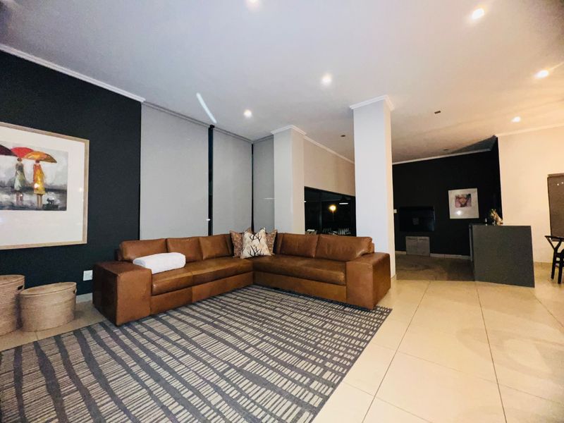 Spacious living area featuring modern tiled flooring, recessed downlighting, and a neutral color palette with a striking dark accent wall.