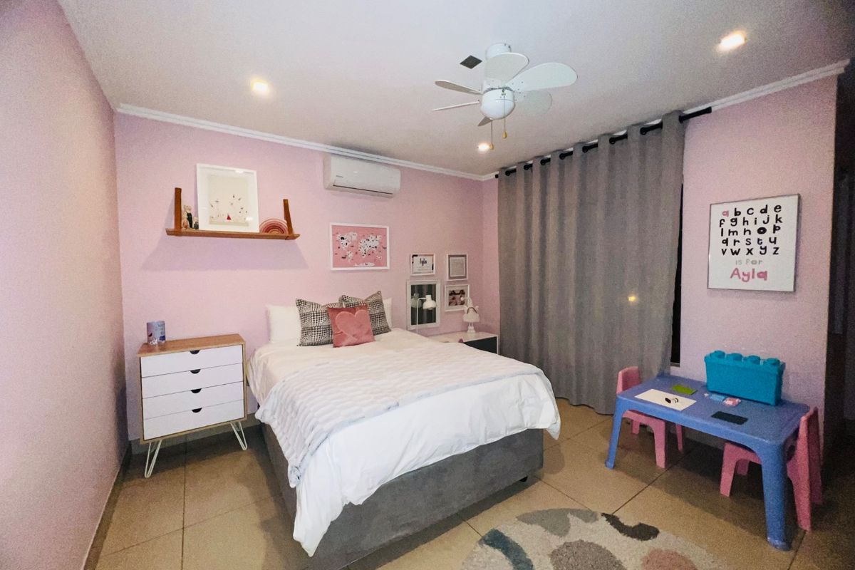 A well-maintained bedroom featuring tiled flooring, a ceiling fan, and a wall-mounted split-system air conditioner.