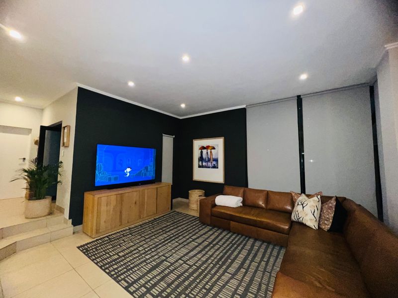 A modern living room featuring tiled flooring, recessed downlighting, and neutral wall finishes with a dark accent wall.