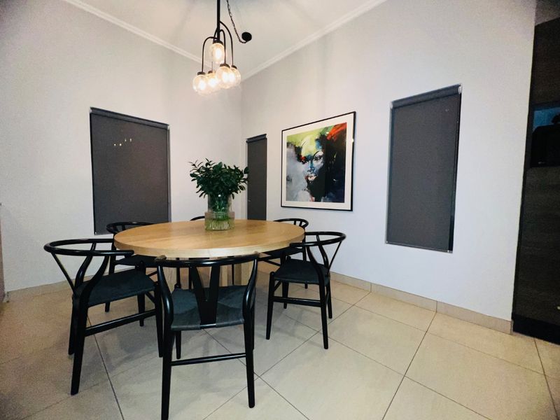 A well-maintained dining area featuring neutral tiled flooring, modern pendant lighting, and roller blinds, creating a clean and contemporary space.