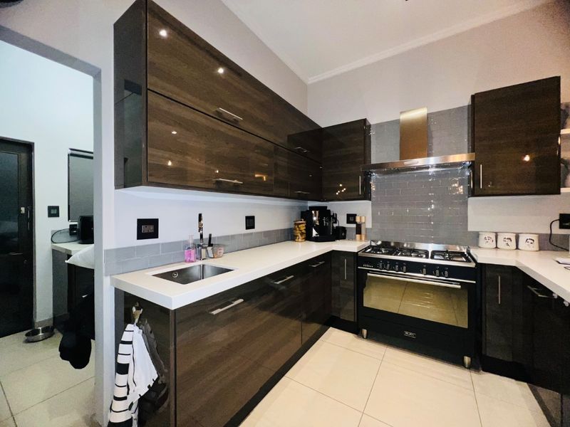 Modern kitchen featuring high-gloss dark cabinetry, white stone countertops, subway tile backsplash, and a stainless steel gas stove with extractor fan.