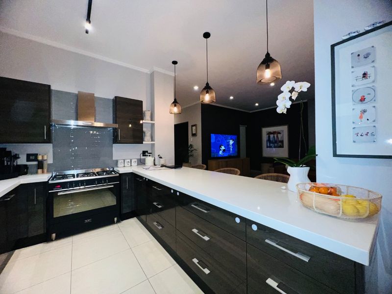 Modern open-plan kitchen featuring dark cabinetry, stone countertops, gas stove with extractor, and stylish pendant lighting, seamlessly flowing into the living area.