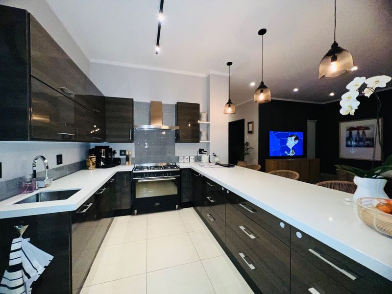 Modern open-plan kitchen featuring high-gloss cabinetry, stone countertops, a gas stove with extractor, and sleek tiled flooring, seamlessly flowing into the living area.
