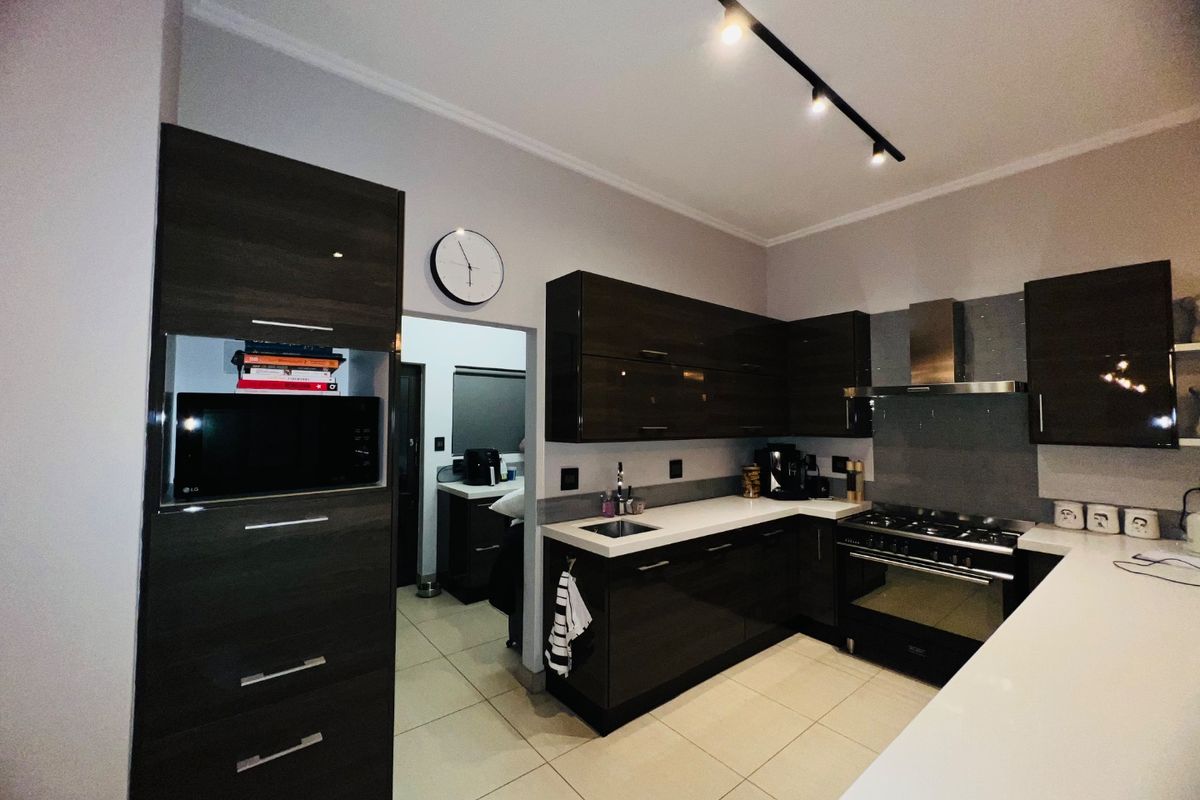 Modern kitchen featuring dark high-gloss cabinetry, white countertops, gas stove with extractor fan, and sleek track lighting.