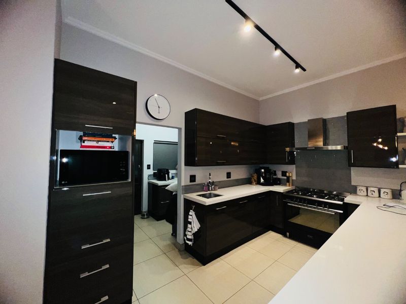Modern kitchen featuring dark high-gloss cabinetry, white countertops, gas stove with extractor fan, and sleek track lighting.