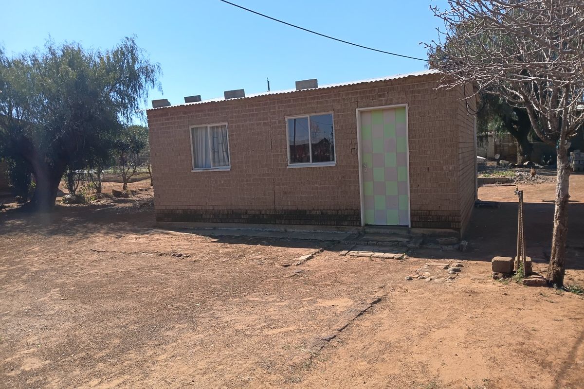 A detached single-story structure featuring exposed brick walls, a corrugated metal roof, and simple window and door fixtures set on a dirt lot.