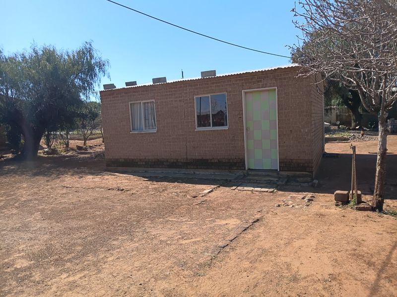 A detached single-story structure featuring exposed brick walls, a corrugated metal roof, and simple window and door fixtures set on a dirt lot.
