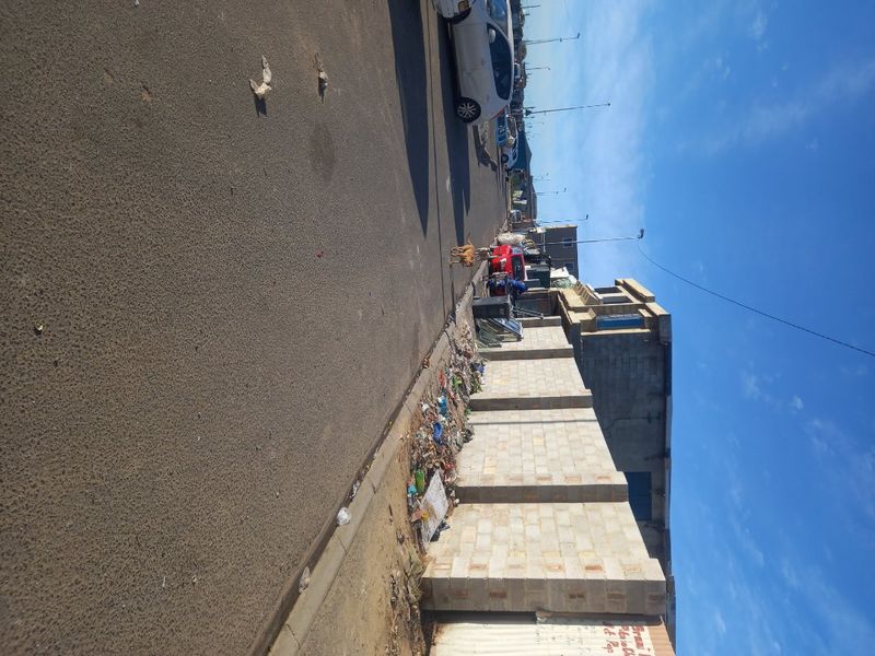 A street-level view of the property boundary, featuring a concrete block wall along an asphalt road with visible debris along the perimeter.