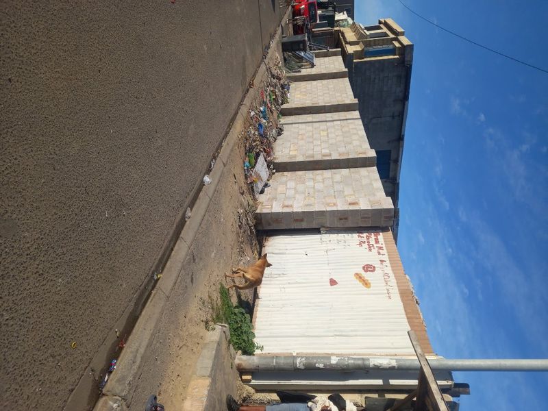 Street view of the property boundary featuring a concrete block wall and corrugated metal fencing along the paved road.
