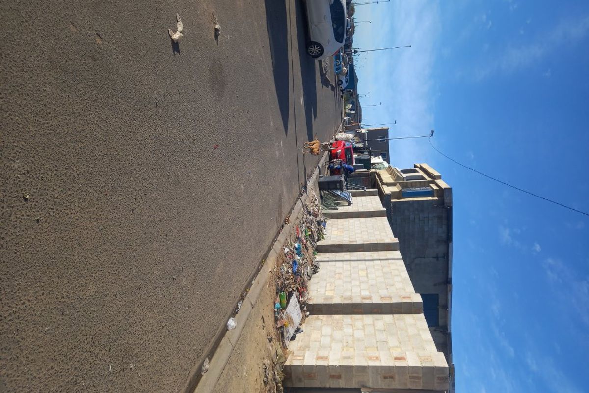 A street-level view of the property boundary, featuring a concrete block wall along an asphalt road with visible debris along the perimeter.