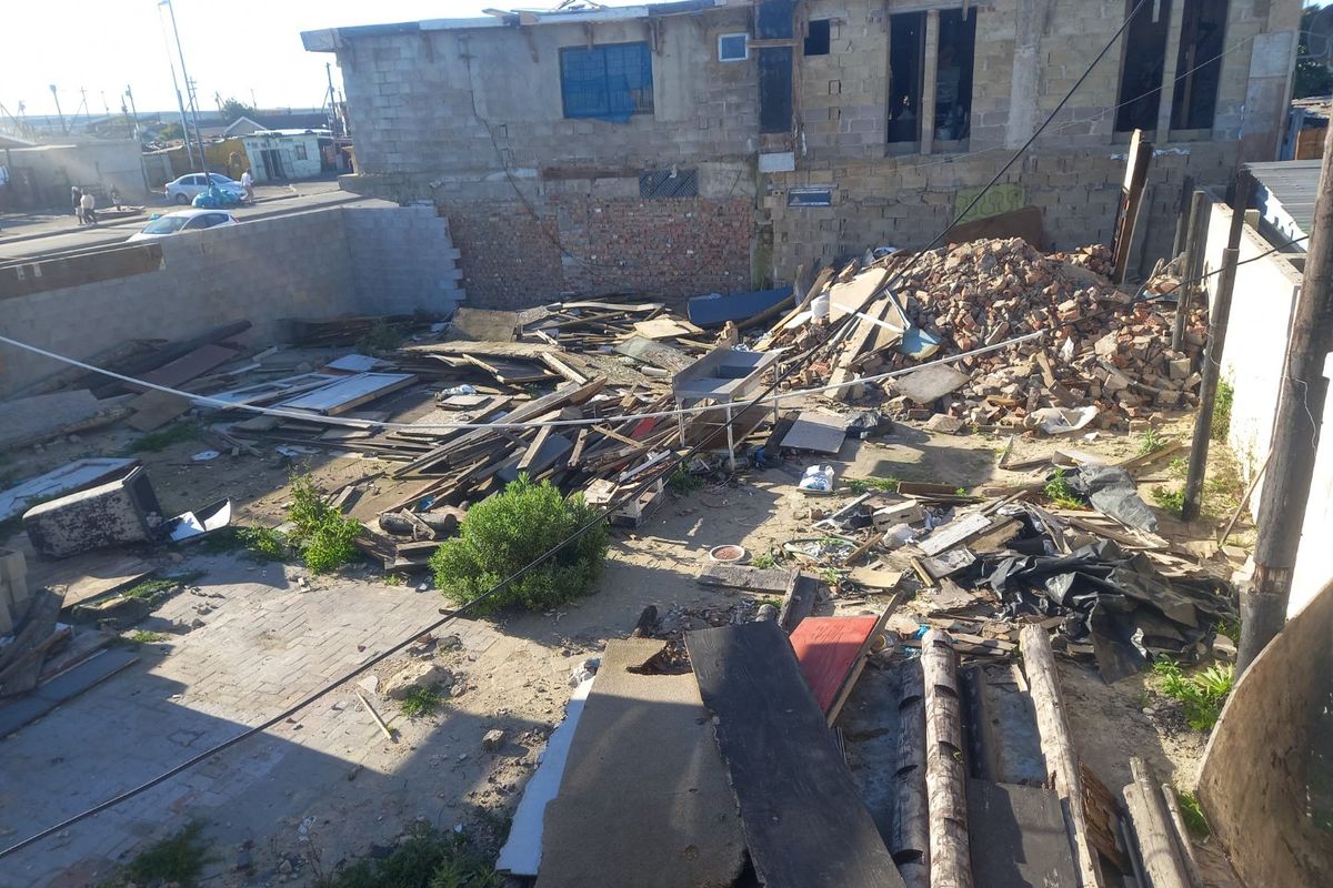 An elevated view of a vacant residential plot featuring significant construction debris, rubble, and unfinished masonry walls requiring extensive site clearance.