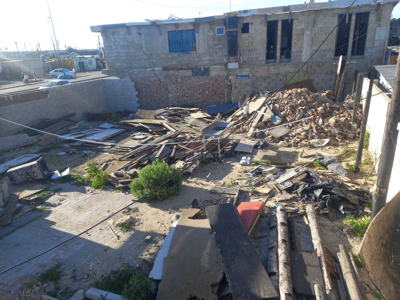 An elevated view of a vacant residential plot featuring significant construction debris, rubble, and unfinished masonry walls requiring extensive site clearance.