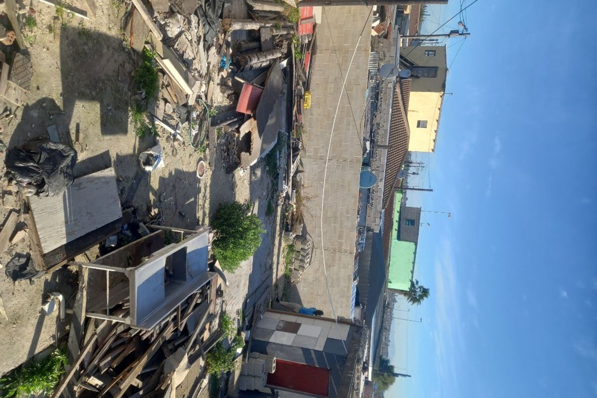 An outdoor area showing a vacant residential plot with significant debris, waste materials, and boundary walling.