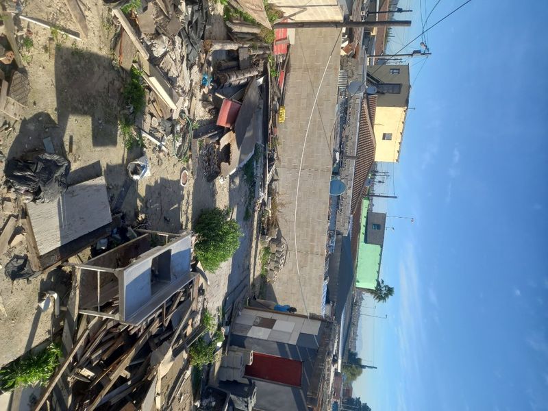 An outdoor area showing a vacant residential plot with significant debris, waste materials, and boundary walling.