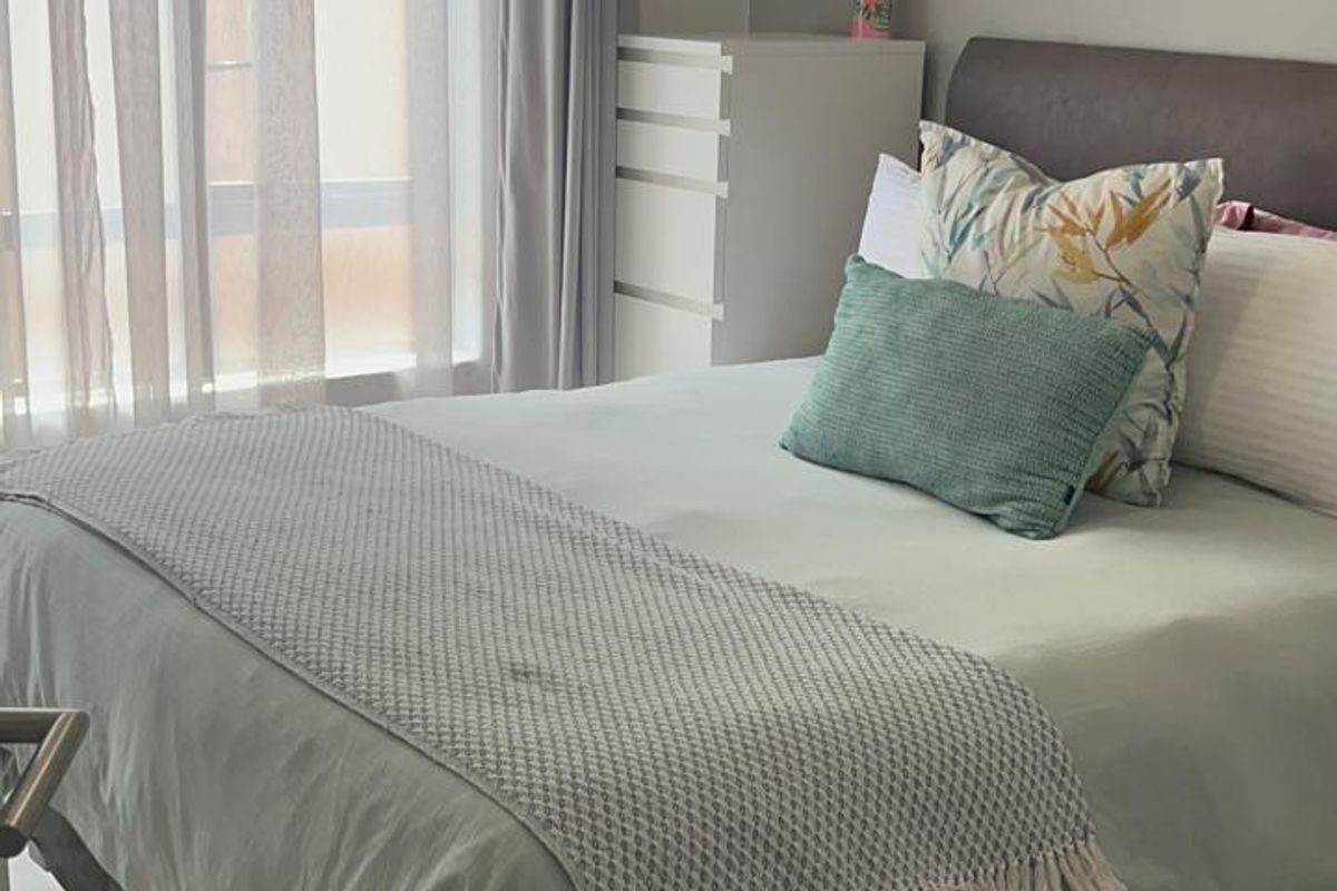 A well-lit bedroom featuring neutral wall tones, tiled flooring, and large windows with installed curtain tracks.