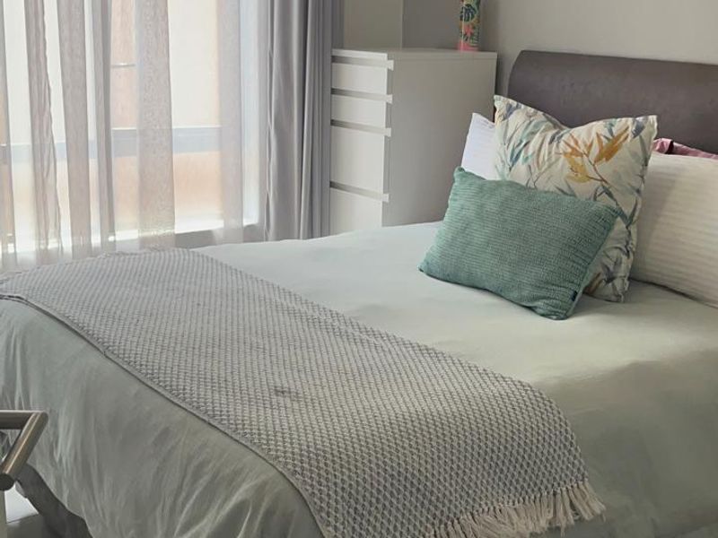 A well-lit bedroom featuring neutral wall tones, tiled flooring, and large windows with installed curtain tracks.