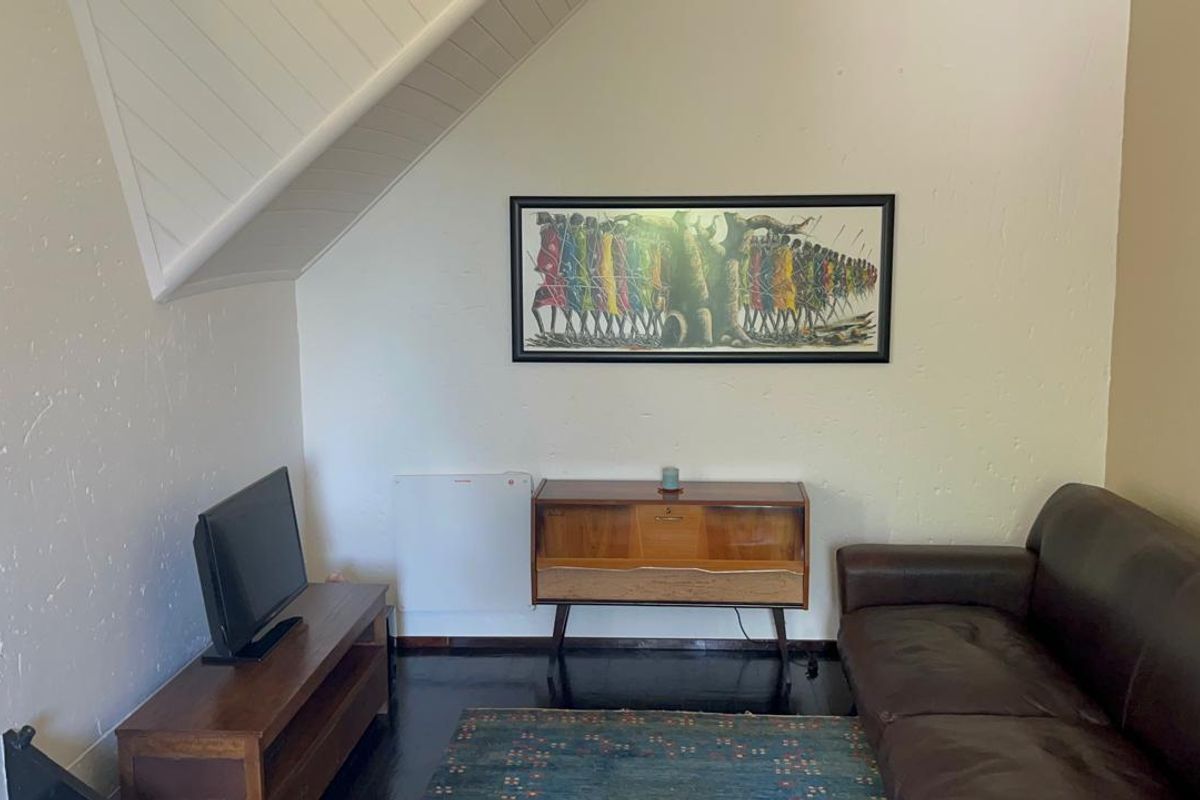 A cozy living room featuring a sloped ceiling, dark timber flooring, and a wall-mounted heater, providing a comfortable and functional living space.