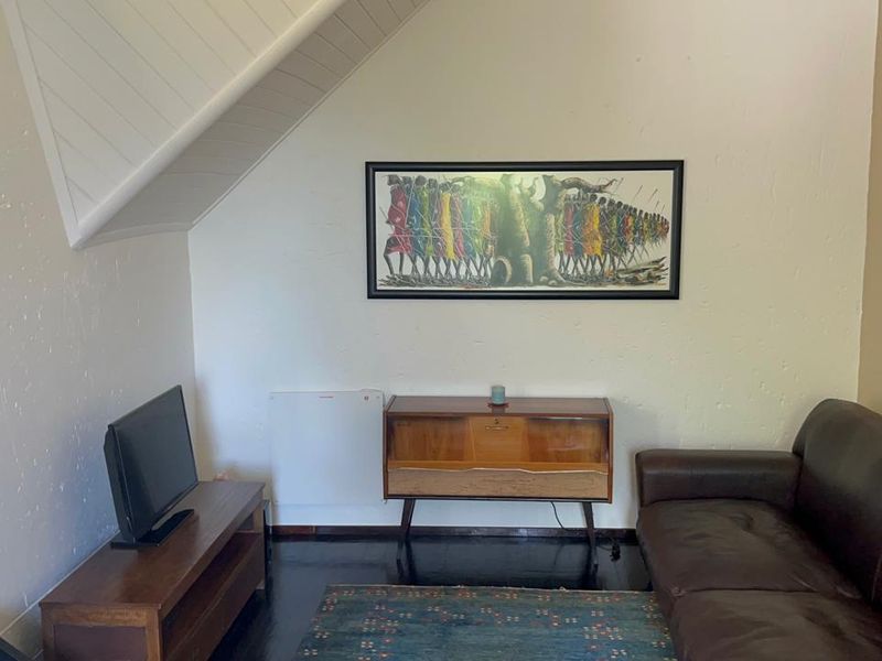 A cozy living room featuring a sloped ceiling, dark timber flooring, and a wall-mounted heater, providing a comfortable and functional living space.