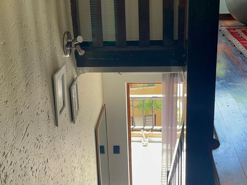 A view looking down a wooden staircase towards an entrance, featuring a wooden balustrade and textured wall finishes.