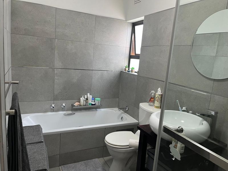 Modern bathroom featuring large-format grey wall tiles, a built-in bathtub, a contemporary basin, and a functional casement window for natural light.