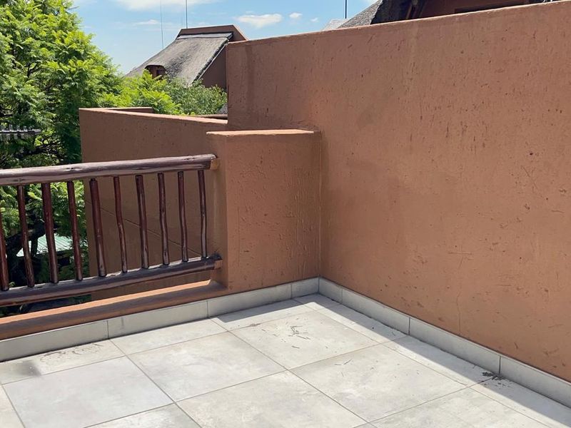 An open-air balcony featuring tiled flooring, a timber balustrade, and plastered masonry walls, offering a private outdoor space.
