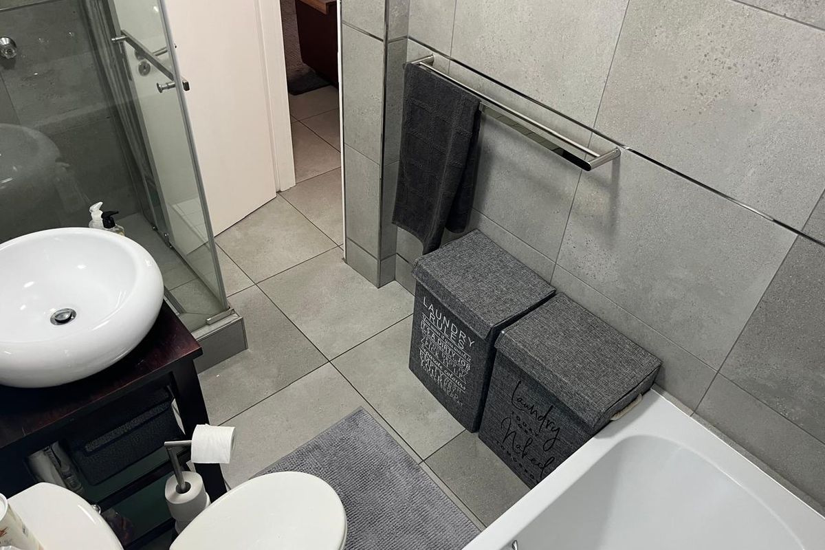 Modern bathroom featuring a vessel sink, glass shower enclosure, bathtub, and neutral grey ceramic tiling throughout.