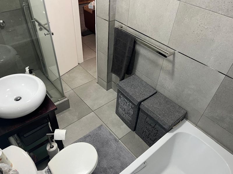 Modern bathroom featuring a vessel sink, glass shower enclosure, bathtub, and neutral grey ceramic tiling throughout.
