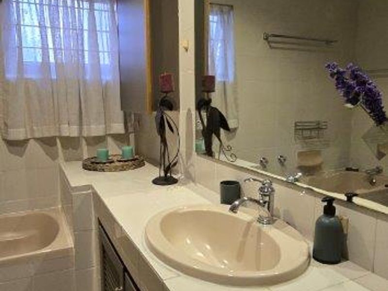 A functional bathroom featuring a tiled vanity with an inset basin, a large wall mirror, and a tiled bathtub area with neutral finishes.