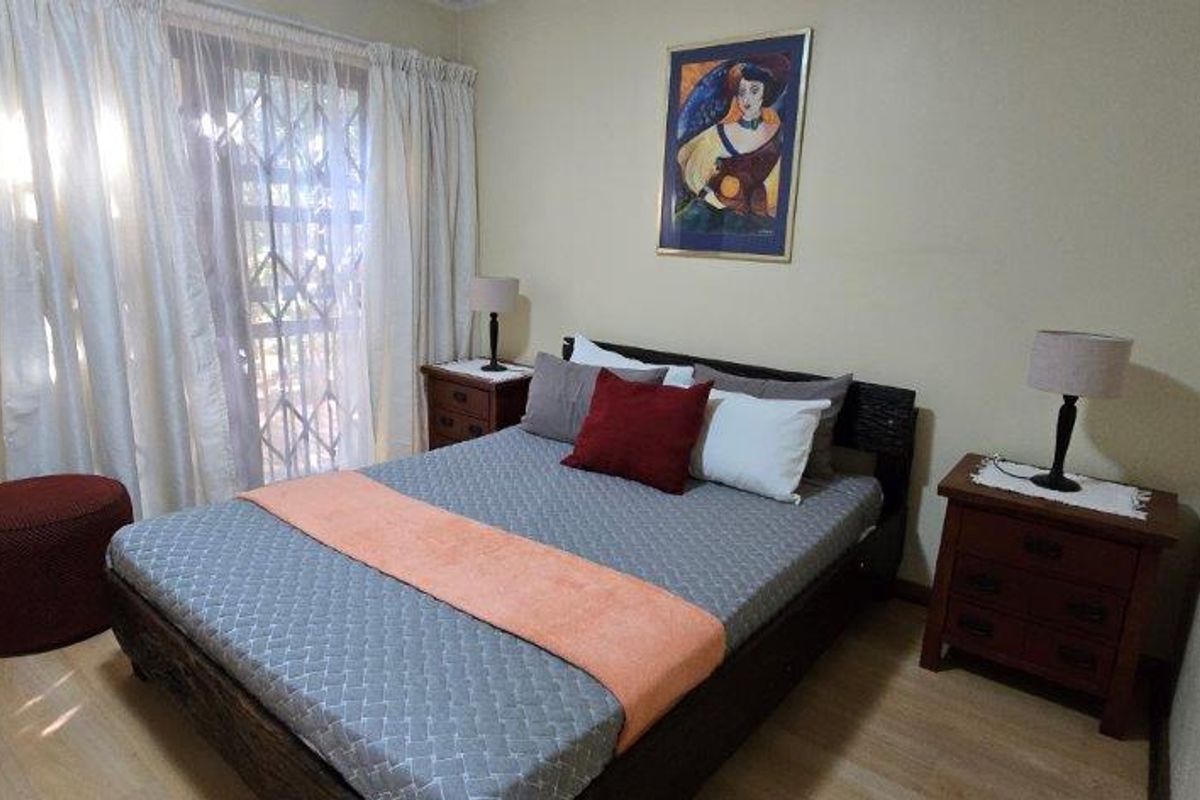 A bedroom featuring laminate flooring and a sliding glass door with an integrated security gate, providing access to the exterior.