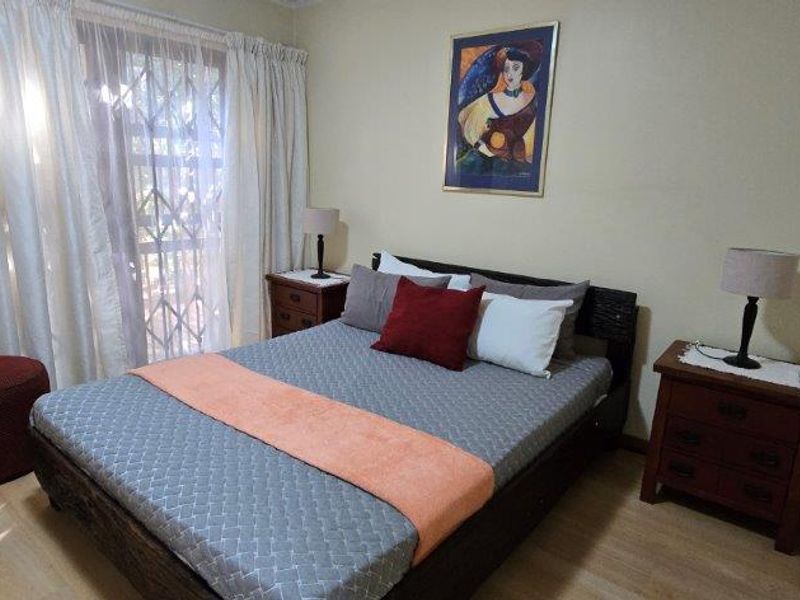 A bedroom featuring laminate flooring and a sliding glass door with an integrated security gate, providing access to the exterior.