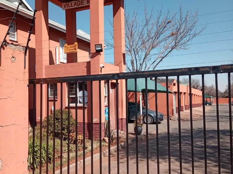Front entrance view of the apartment complex featuring a security gate, guard house, and paved driveway with covered parking bays.