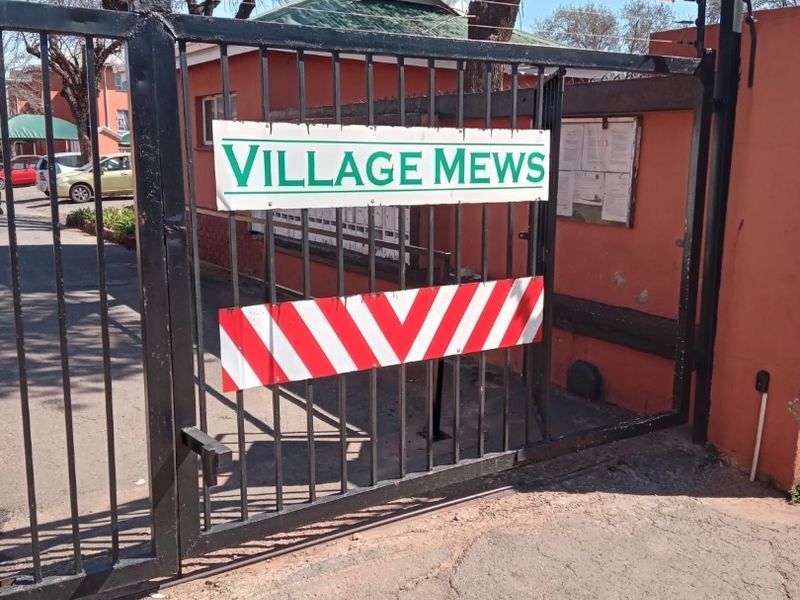 The main entrance gate to the Village Mews apartment complex, featuring secure metal fencing and perimeter security infrastructure.