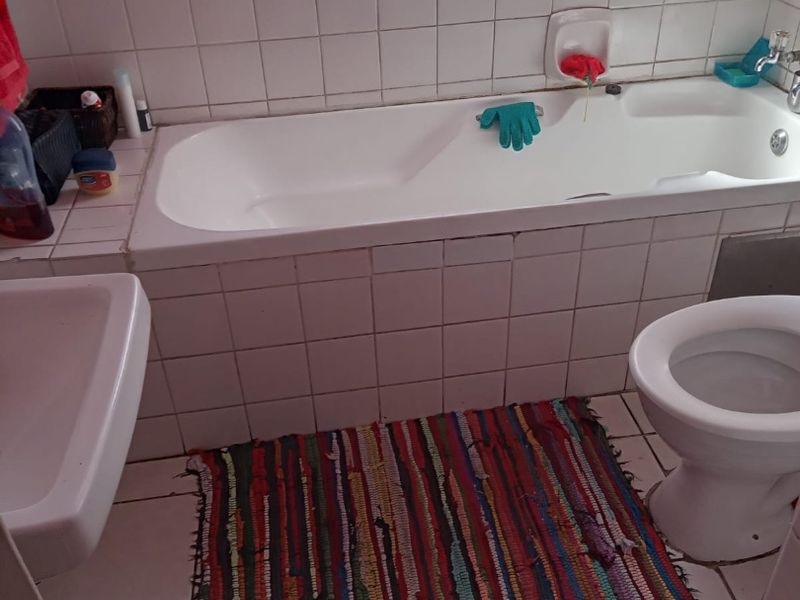 A functional bathroom featuring a standard bathtub, toilet, and washbasin with white wall tiling and floor tiles.