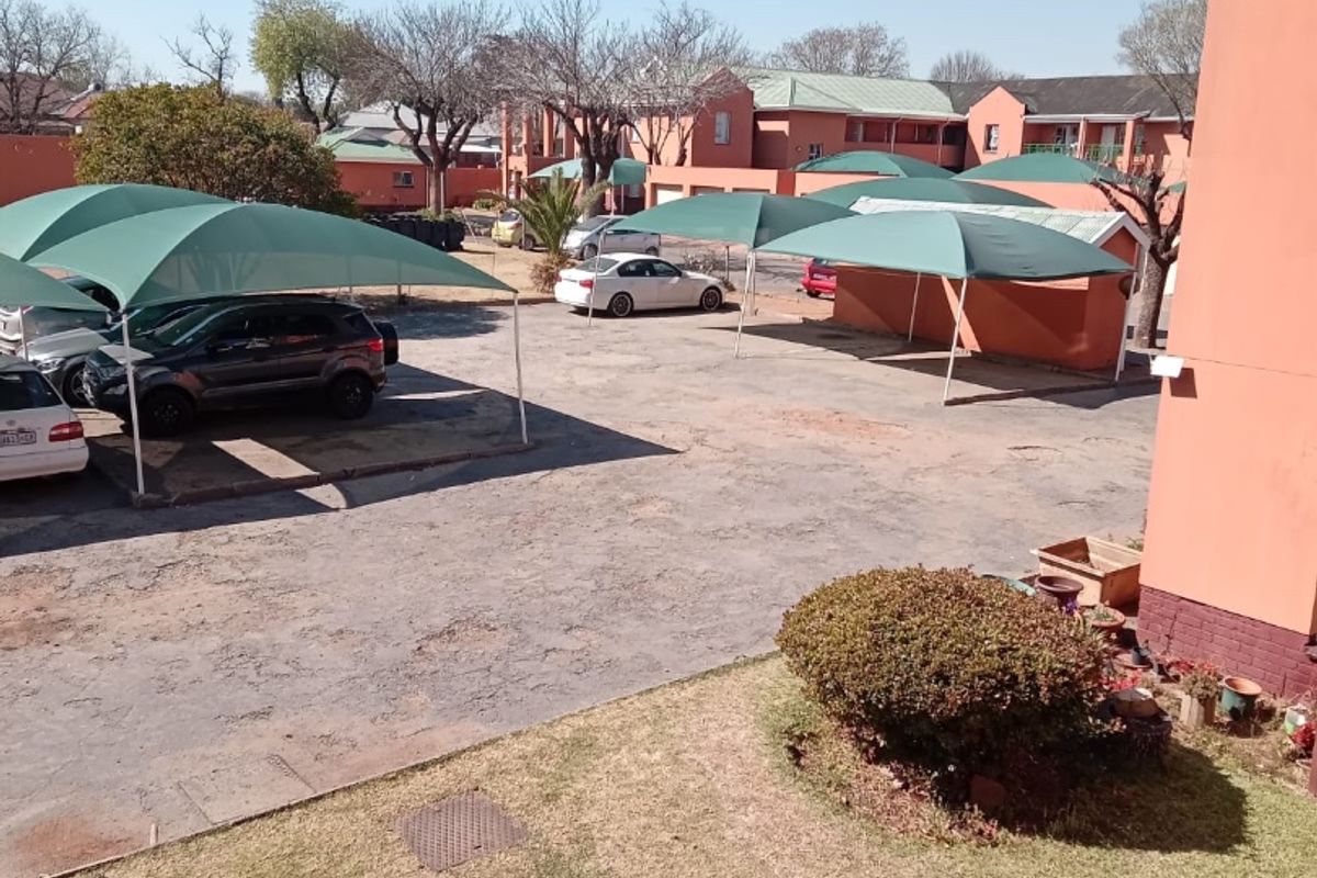 View of the apartment complex rear parking area featuring shade cloth carports and communal garden space.