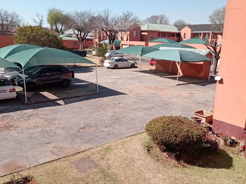 View of the apartment complex rear parking area featuring shade cloth carports and communal garden space.