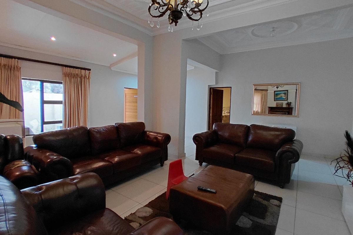 Spacious living room featuring tiled flooring, ornate ceiling detailing, and a central chandelier, offering a bright and open layout.